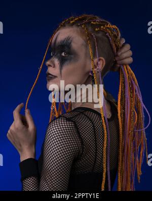 Drammatico ritratto di giovane donna con horror nero palco trucco dipinto sul viso e colore arancione Dreadlocks acconciatura. Studio girato su sfondo blu Foto Stock