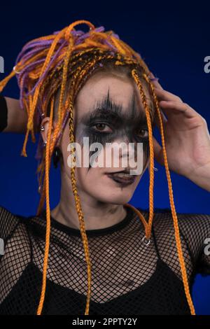 Giovane donna informale con capelli colorati Dreadlocks e horror nero palco make up dipinto sul viso. Studio girato su sfondo blu. Parte della foto Foto Stock