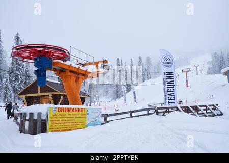 Iogach, Russia - 10 marzo 2018: Stazione sciistica invernale Teletsky Altai. Seggiovia Clasp sul monte e sullo sfondo della foresta sotto le nevicate. L'iscrizione Foto Stock