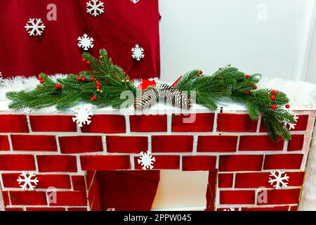 Il camino decorativo è decorato con rami di albero di Natale e coni Foto Stock