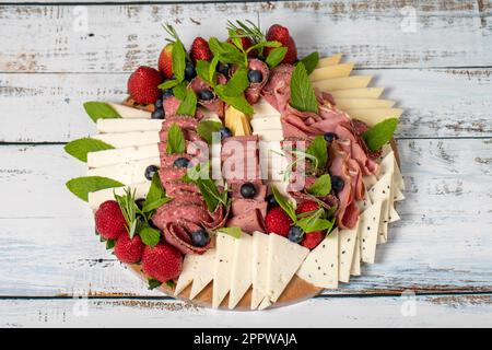 Set di piastre antipasto. Piatto di carne affumicata fredda. Antipasto con prosciutto, prosciutto, salame, formaggio azzurro, mozzarella con mirtilli e fragole Foto Stock