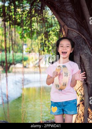 Bambina asiatica giocare il tamburello, nel giardino sotto il grande albero Foto Stock