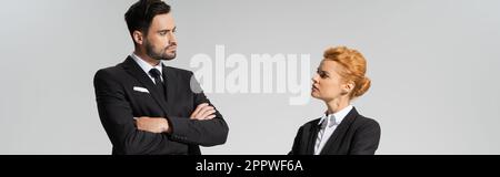 seri e scettici uomini d'affari che si guardano l'un l'altro in piedi con braccia incrociate isolato su grigio, banner, immagine stock Foto Stock