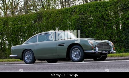 Bicester, Oxon, Regno Unito - Aprile 23rd 2023. 1965 verde Aston Martin DB5 viaggiando su una strada di campagna inglese Foto Stock