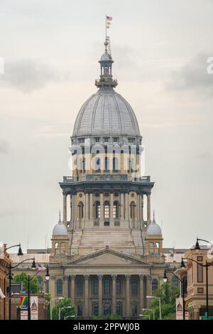 Il cupo grigio del Campidoglio dello Stato dell'Illinois e la sua alta lanterna, con una bandiera in cima, si ergono dietro una strada fiancheggiata da lampioni a Springfield, Illinois. Foto Stock