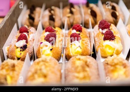 Primo piano di una bella e vivace esposizione di pasticcini francesi attraverso una finestra di panetteria, ciambelle aperte Foto Stock