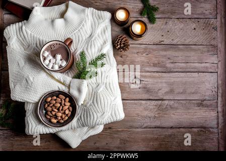 Bevanda calda del caffè, mandorle, maglione lavorato a maglia accogliente su fondo di legno con candele, rami di abete e coni, spazio copia. Hygge e concetto di comfort domestico. Foto Stock