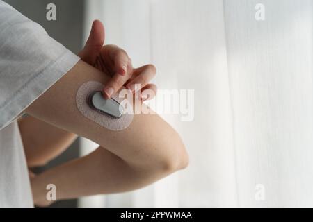 Primo piano di una donna che fissa un monitor per la glicemia continuo al braccio Foto Stock