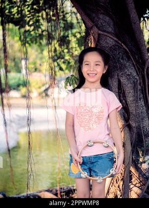 Bambina asiatica giocare il tamburello, nel giardino sotto il grande albero Foto Stock