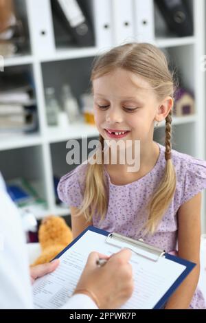 Amichevole medico pediatra donna che tiene appunti ascoltando la bambina Foto Stock