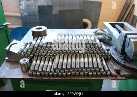 Molti borchie in metallo lucido con intaglio, dadi, anelli in ferro, guarnizioni, utensili in metallo e morsa industriale sul tavolo in fabbrica, negozio. Foto Stock