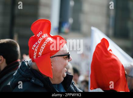 Strasburgo, Francia - Mar 29, 2023: Un anziano sorridente sta in piedi fra una folla di uomini adulti ad una protesta francese, portando un cappello con un messaggio importante a t Foto Stock