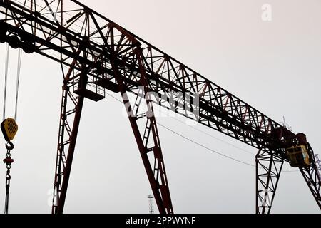 Gru industriale a portale in ferro grande metallo con gancio montato sui supporti per il sollevamento e il trasporto di carichi pesanti, spostandosi di fatto lungo le rotaie Foto Stock