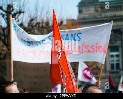 Strasburgo, Francia - 29 marzo 2023: Un gruppo di manifestanti adulti si radunano all'esterno di un grande edificio architettonico, tenendo bandiere e cartelli con testo prot Foto Stock