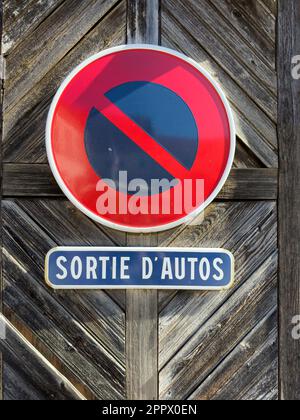 Un cartello rosso vintage avverte di uscire auto in un moderno garage urbano, la sua entrata francese della città illuminata dalla luce e circondata da cancelli di legno Foto Stock