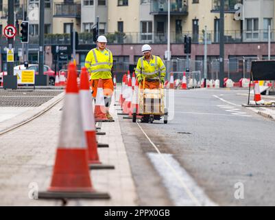 Due operai dipingono linee bianche sulla strada accanto ai binari del tram, Leith, Edimburgo, Scozia, Regno Unito Foto Stock