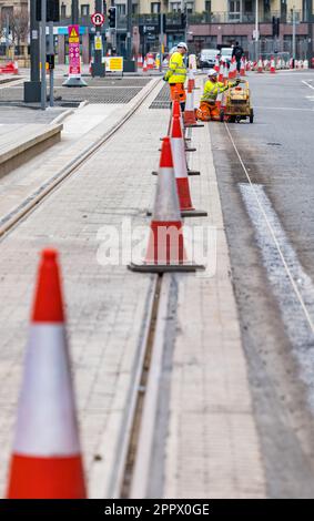 Due operai dipingono linee bianche sulla strada accanto ai binari del tram, Leith, Edimburgo, Scozia, Regno Unito Foto Stock