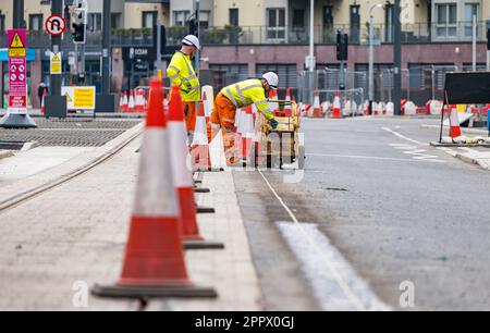 Due operai dipingono linee bianche sulla strada accanto ai binari del tram, Leith, Edimburgo, Scozia, Regno Unito Foto Stock