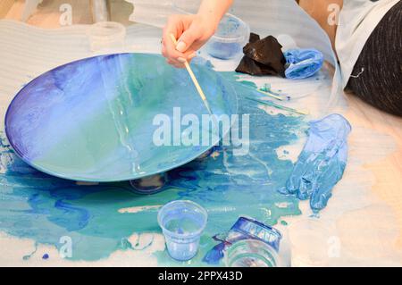 Il processo di creazione di un disegno moderno astratto fatto in casa dipinto con un pennello di resina multicolore blu acrilico su un asse di legno rotondo. Foto Stock