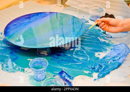 Il processo di creazione di un disegno moderno astratto fatto in casa dipinto con un pennello di resina multicolore blu acrilico su un asse di legno rotondo. Foto Stock