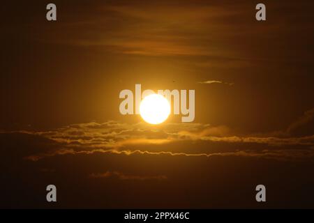 Un tramonto arancione mozzafiato che si riflette su nuvole bianche e grigie in un cielo scuro Foto Stock