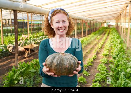 Ritratto di femmina sorridente contadina matura che tiene zucca appena raccolta in piedi in serra Foto Stock