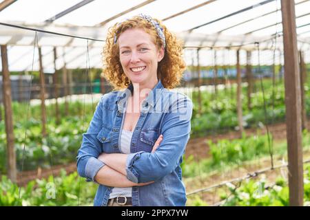 Ritratto di sicura agricoltrice con le braccia incrociate in piedi in fattoria Foto Stock