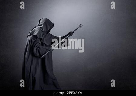 Wizard con cappuccio con cappuccio e magiche persone su sfondo oscuro e misterico Foto Stock