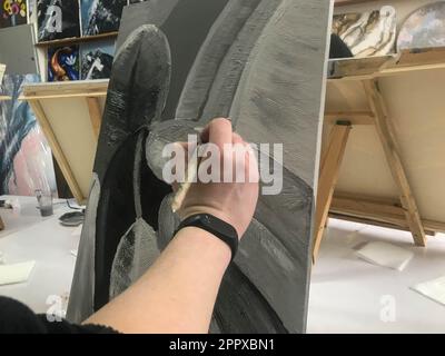 La mano di un artista dipinge un'immagine creativa in bianco e nero con un pennello su tela in un laboratorio. Foto Stock