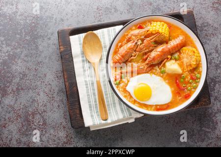 Chupe de Camarones Pesce padella peruviana Pesce zuppa con pomodori, mais, pepe, patate, piselli verdi e primo piano delle uova su una ciotola sul tavolo. Orizzontale in alto v Foto Stock