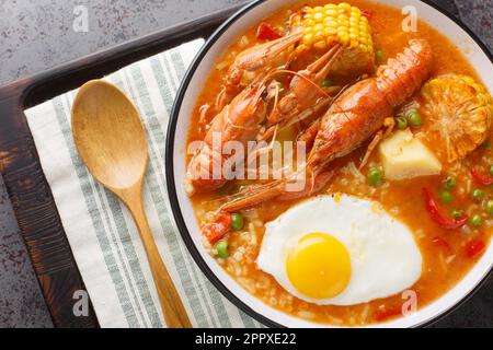 Zuppa spessa con gamberi, pomodori, mais, pepe, patate, piselli verdi e primo piano dell'uovo in una ciotola sul tavolo. Vista orizzontale dall'alto Foto Stock