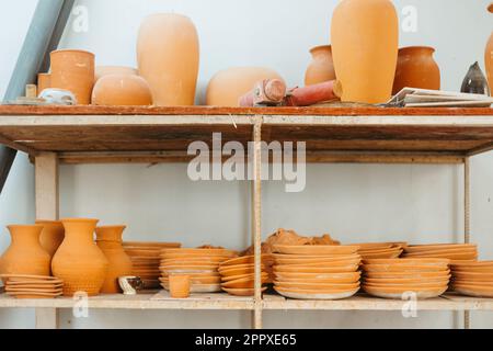 Raccolta di vari vasi in argilla fatti a mano e diverse piastre disposte su scaffali su fondo bianco in officina Foto Stock