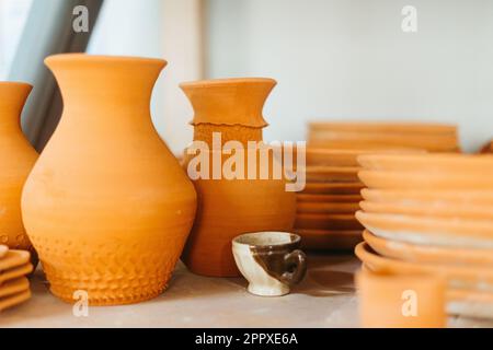 Vari vasi di argilla e piastre in ceramica posti su scaffale su sfondo bianco vicino alla tazza Foto Stock