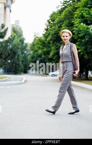 Ritratto lunghezza intera di buona donna che cammina all'aperto lungo il sentiero tra piante verdi. Ben vestito di mezza età, 40s signora. Spazio libero per la copia Foto Stock