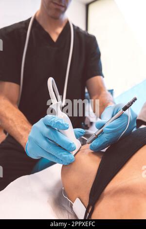 Medico irriconoscibile in guanti di lattice trattamento del paziente con apparecchiature a ultrasuoni durante l'esame del braccio durante la nomina in ospedale contemporaneo Foto Stock