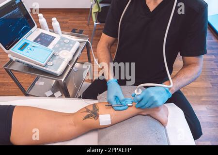 Medico irriconoscibile in guanti di lattice che trattano il paziente con apparecchiature a ultrasuoni durante l'esame della gamba durante l'appuntamento in ospedale contemporaneo Foto Stock