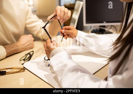 Corto irriconoscibile giovane cliente maschile consulenza con oftalmologo femminile, mentre la scelta occhiali in negozio ottico Foto Stock