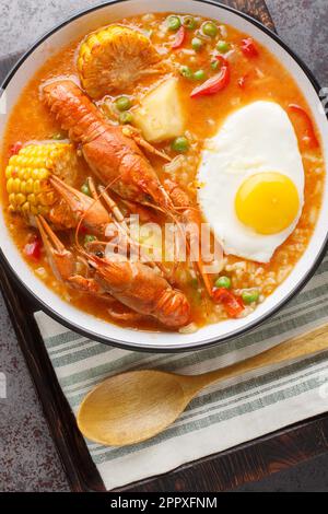 Zuppa di gamberi con pomodori, mais, pepe, patate, piselli verdi e primo piano con uova in un recipiente sul tavolo. Vista verticale dall'alto Foto Stock