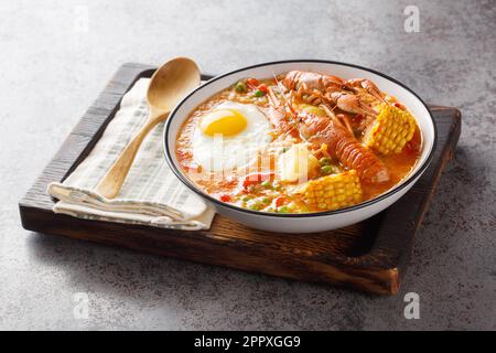 Chupe de Camarones Pesce padella peruviana Pesce zuppa con pomodori, mais, pepe, patate, piselli verdi e primo piano delle uova su una ciotola sul tavolo. Orizzontale Foto Stock