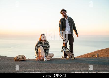 Corpo pieno di diversi giovani e donne felici con skateboard e in abiti casual sorridendo e guardando la macchina fotografica mentre si passa di nuovo insieme Foto Stock