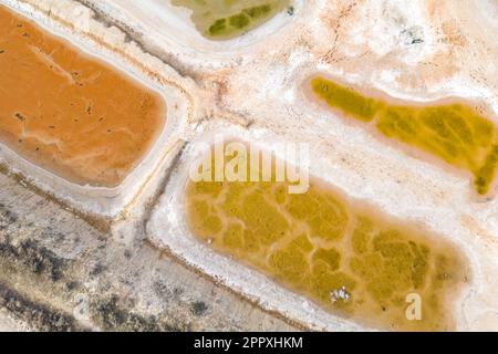 Vista mozzafiato delle lagune colorate con i bordi cristallizzati di sale bianco e l'area secca e scura che circonda i corpi di acqua salata arancione e verdastra di giorno Foto Stock