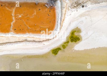 Vista mozzafiato delle lagune colorate con i bordi cristallizzati di sale bianco e l'area secca e scura che circonda i corpi di acqua salata arancione e verdastra di giorno Foto Stock