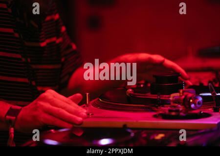 Vista laterale di un DJ maschio anonimo raccolto che suona musica su console professionale durante la festa notturna con luce rossa al neon Foto Stock