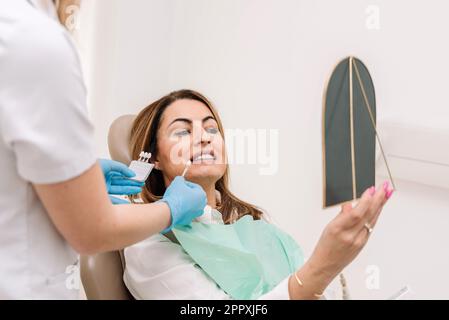 Dentista irriconoscibile in guanti di lattice che dimostrano le veneers dentali durante il lavoro con il paziente durante il trattamento medico Foto Stock