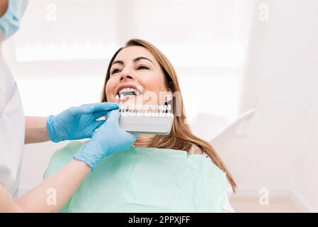 Dentista irriconoscibile in guanti di lattice che dimostrano le veneers dentali durante il lavoro con il paziente durante il trattamento medico Foto Stock