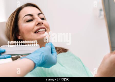 Dentista irriconoscibile in guanti di lattice che dimostrano le veneers dentali durante il lavoro con il paziente durante il trattamento medico Foto Stock