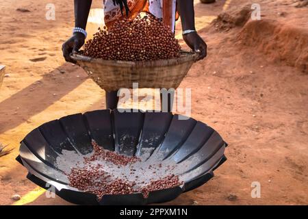 Dall'alto del raccolto anonimo africano femmina che mescola i chicchi di caffè nel cestino di vimini mentre arrostendo su terra sabbiosa Foto Stock