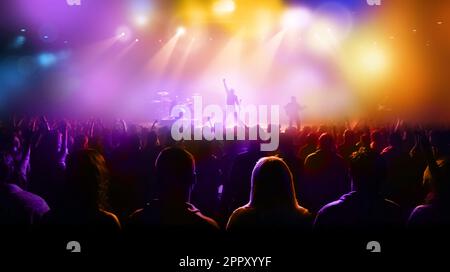 Le sagome di concerti rock si affollano di fronte a luci di scena colorate e luminose Foto Stock