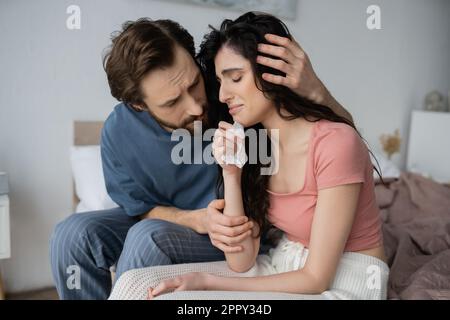 Uomo attento in pajama hugging piangendo e girlfriend rovesciato sul letto a casa, immagine di scorta Foto Stock