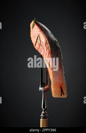 Salmone affumicato su una forchetta. Pezzo di pesce su sfondo nero. Foto Stock